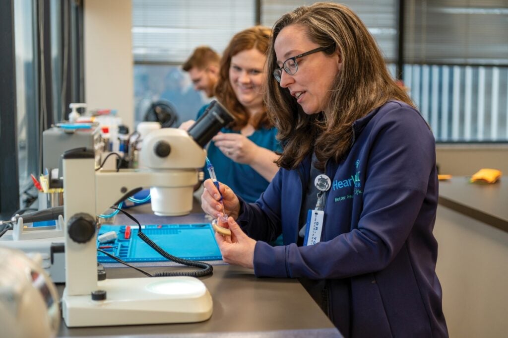 Two women with long medium brown hair sit at a table with microscopes and other lab equipment