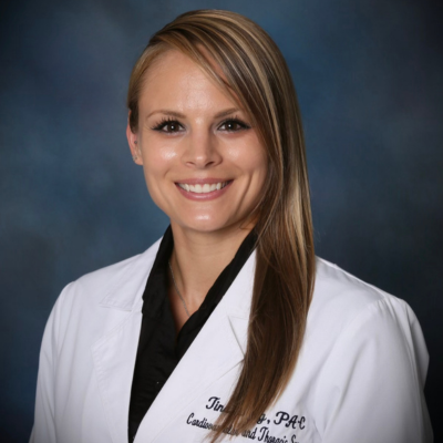 woman with long brown hair with blonde highlights wearing a white lab coat smiles at the camera