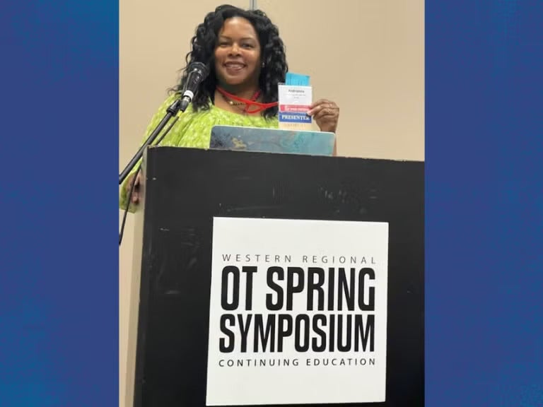 A woman with dark curly hair wearing a green blouse stands at a podium that reads "Western Regional OT Spring Symposium Continuing Education."