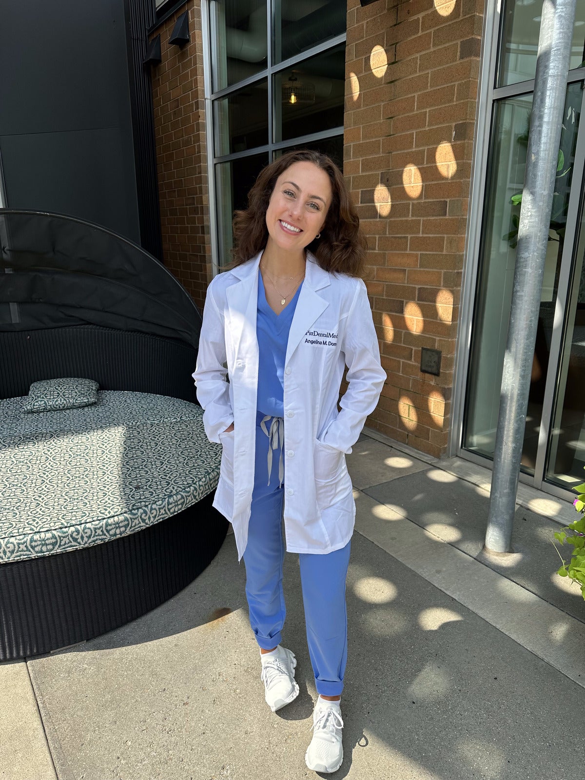 Woman with brown hair wearing blue scrubs, white sneakers and a white lab coat.