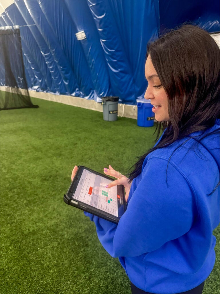 Woman with brown hair wearing a blue hoodie using a tablet.