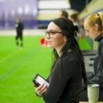 Woman with dark brown hair clipped in the back wearing glasses and a black long sleeve shirt holding a tablet while looking onward.