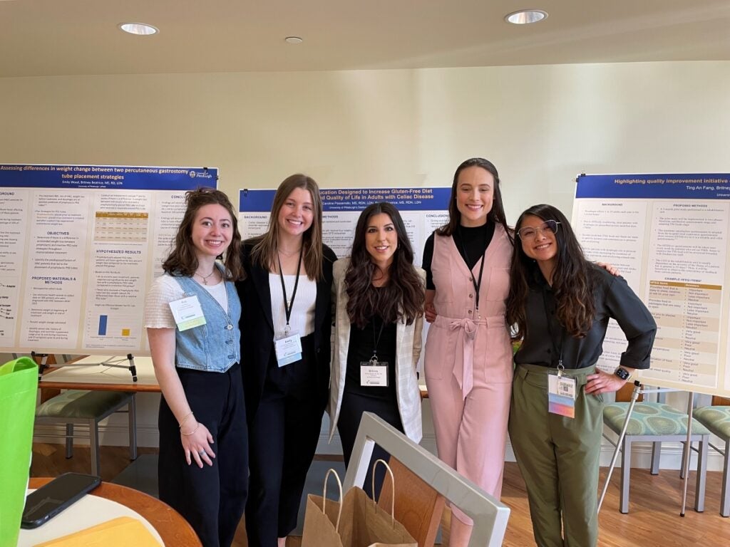 A group of five women standing together in front of three large poster boards.