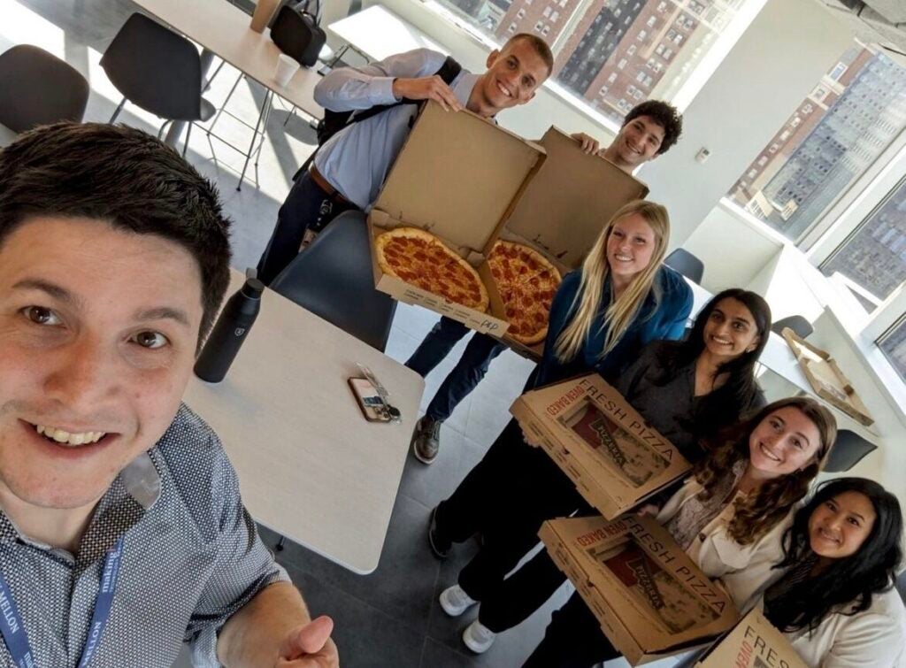 A group of men and women standing together holding boxes of pepperoni pizzas.