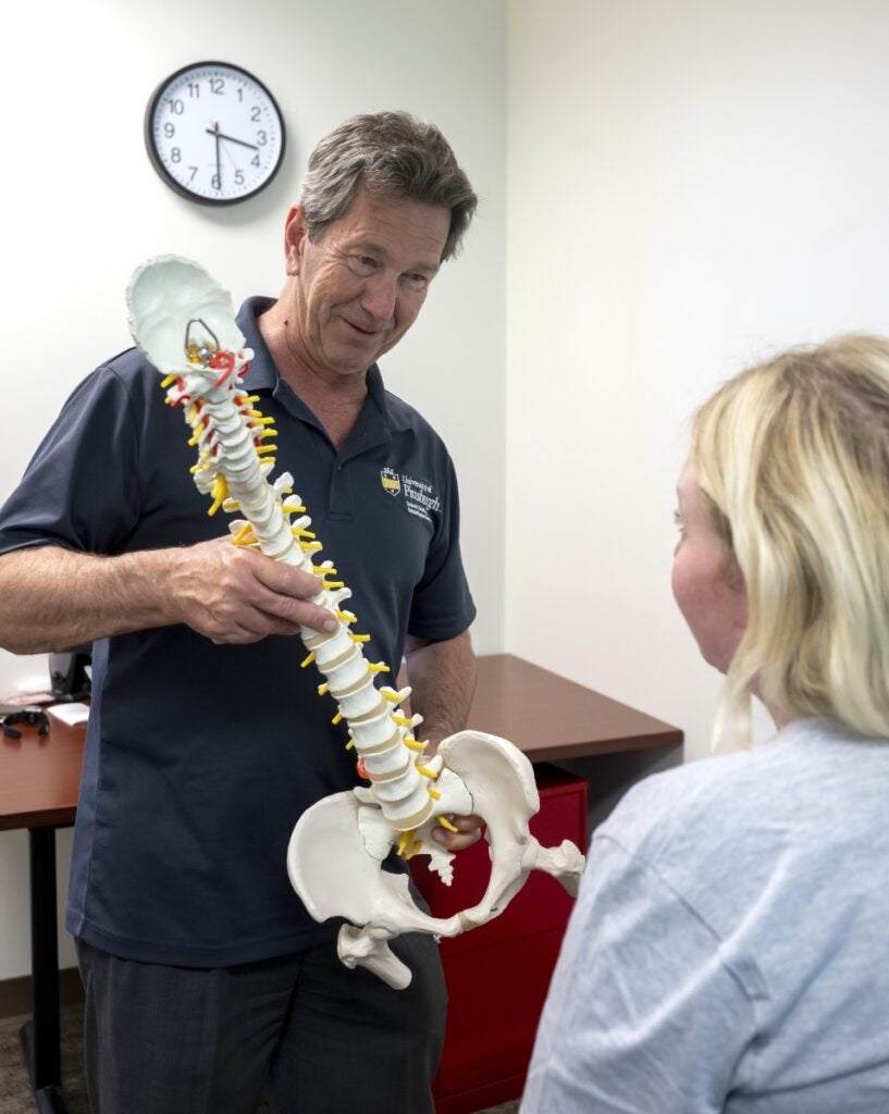 Faculty member holding a model of the human spine in front of a student