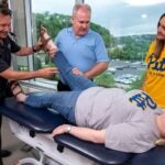 Faculty demonstrate chiropractic maneuvers on patient laying on table while a student watches