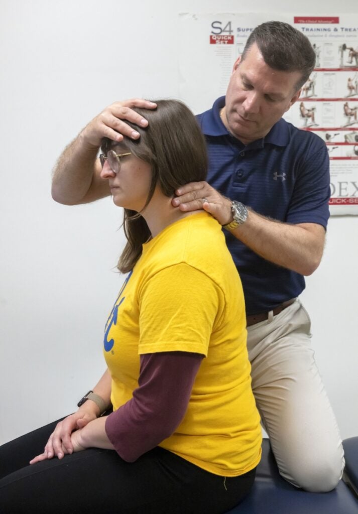 Faculty member standing behind a student to demonstrate a method of examining the joints and muscles of the neck.