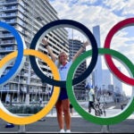 Christie-Lee-Coad standing in the center of a sculpture of the Olympic rings with her hands raised in the air