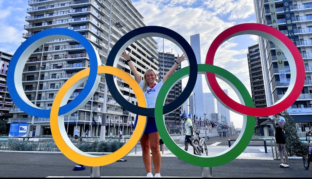 Christie-Lee-Coad standing in the center of a sculpture of the Olympic rings with her hands raised in the air