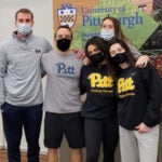 A group of men and woman wearing Pitt gear and face masks standing together.