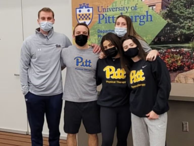 A group of men and woman wearing Pitt gear and face masks standing together.