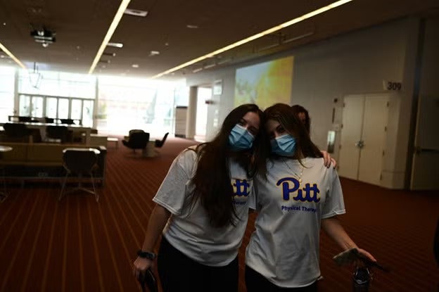 Two women with dark hair wearing white Pitt shirts standing together.