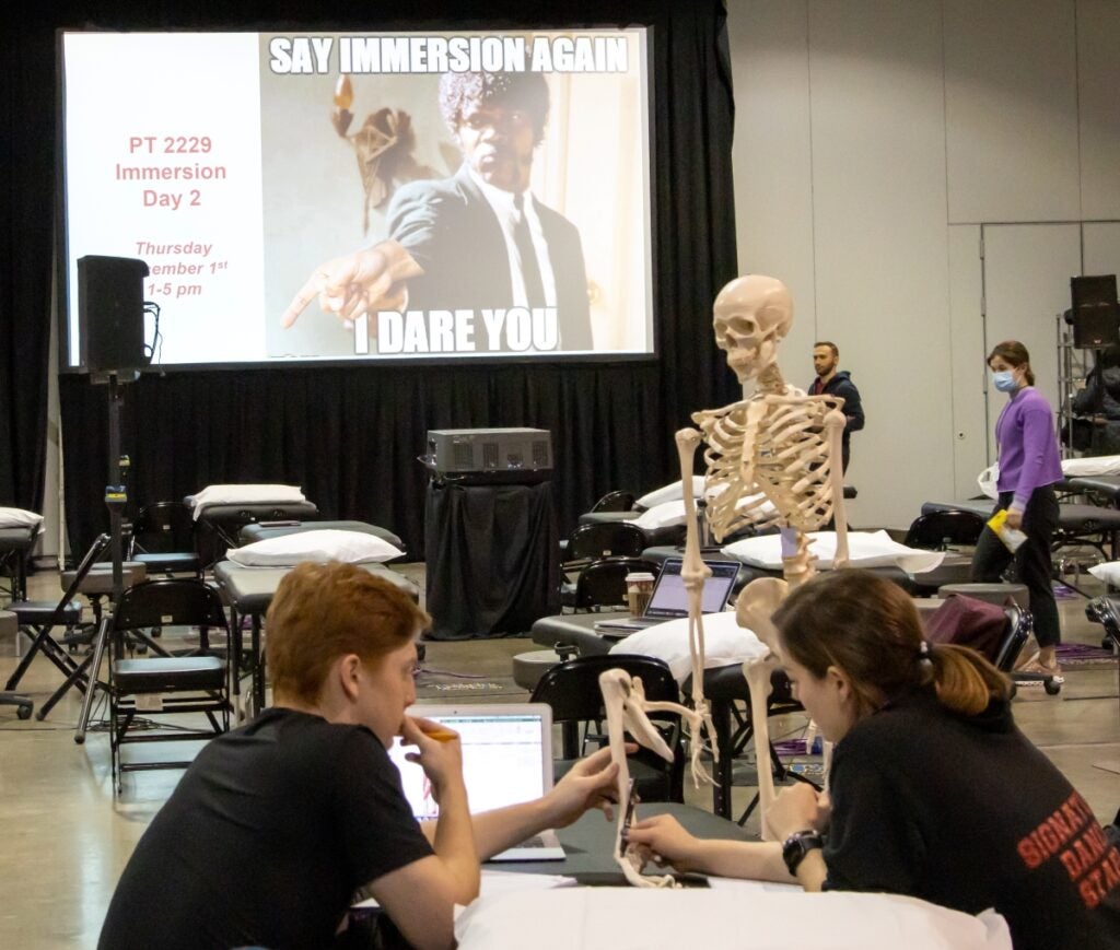 A man with red hair wearing a black shirt and a woman with brown hair wearing a black shirt sitting together examining a skeleton.