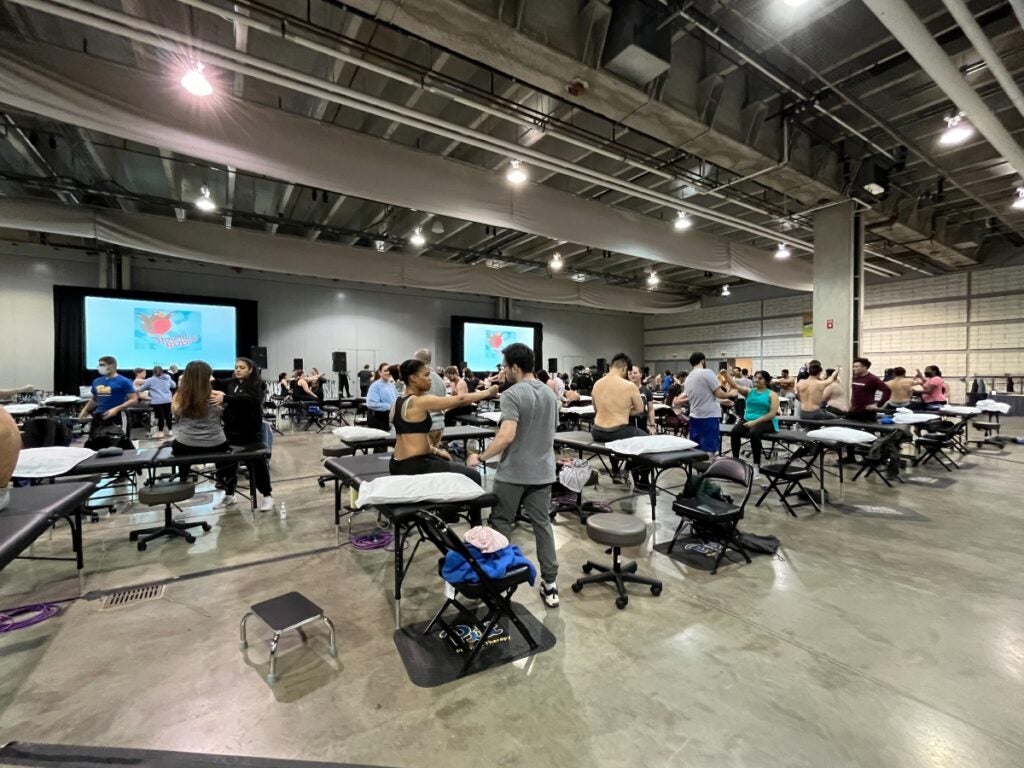 A room full of various black tables where men and women are sitting and standing, examining each other.