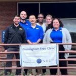 A group of men and women standing together outside in front of a Birmingham Free Clinic sign.