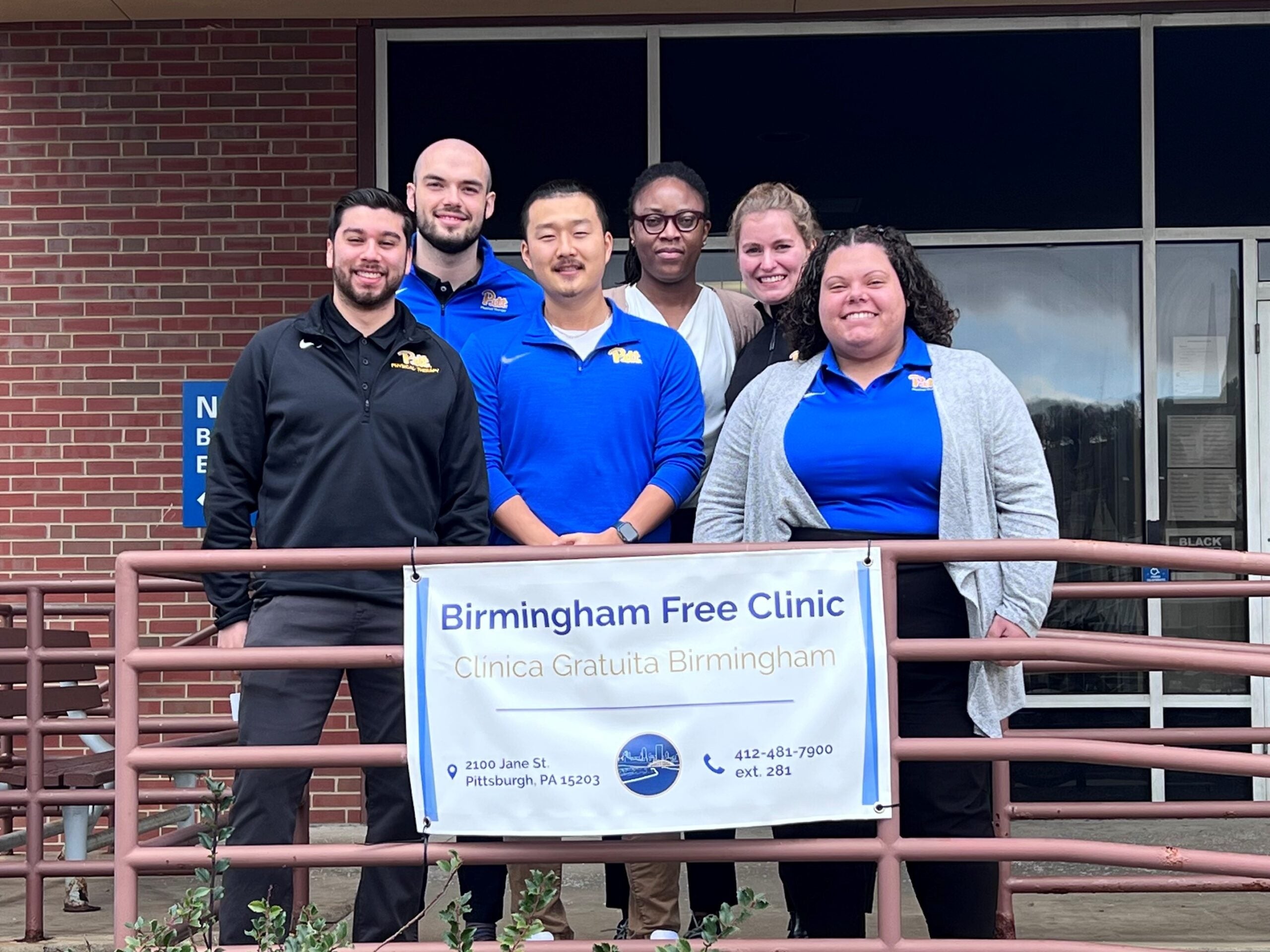 A group of men and women standing together outside in front of a Birmingham Free Clinic sign.