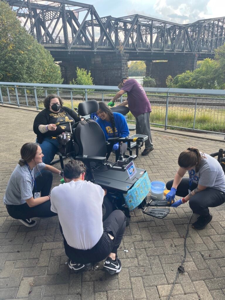 A group of men and women working on a wheelchair outside.