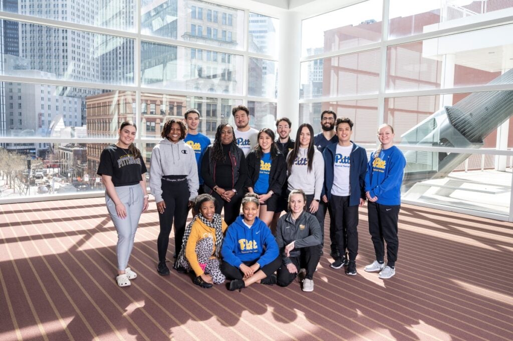 A group of men and women wearing Pitt gear standing together in a well-lit room.