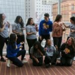 A group of men and women standing together laughing while wearing Pitt gear and holding stethoscopes.