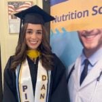 Woman with long brown hair wearing a graduation cap and gown with academic cords, including one that reads "Pitt Dance."