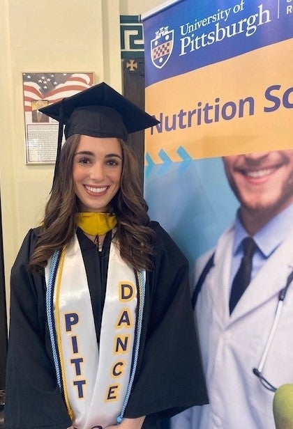 Woman with long brown hair wearing a graduation cap and gown with academic cords, including one that reads "Pitt Dance."