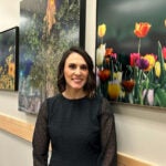 A woman with short, dark brown hair wearing a black blouse with sheer sleeves and black polka dots.