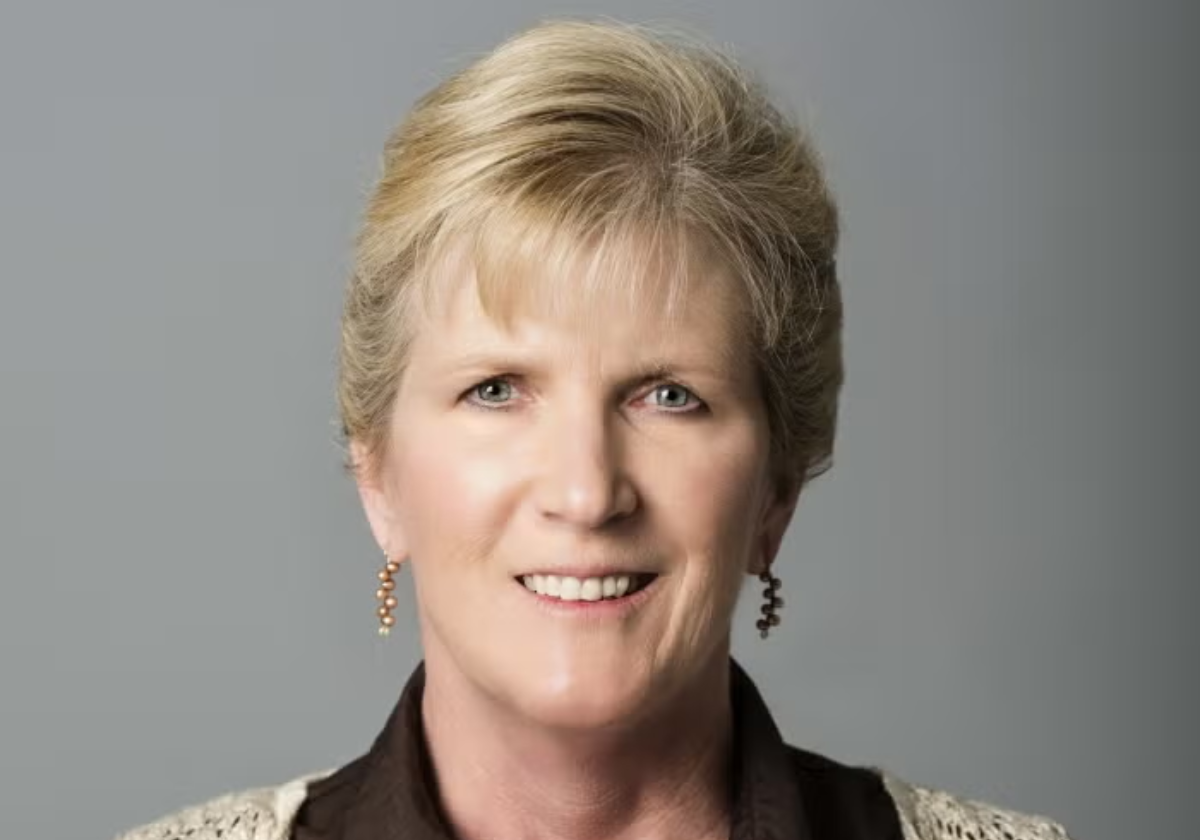 Woman with short blonde hair wearing a white crochet cardigan over a brown collared blouse.