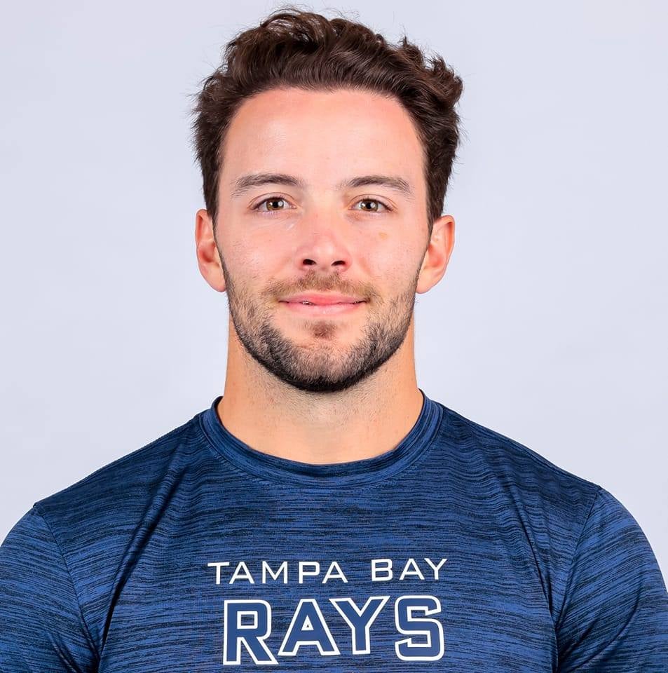 A man with short brown hair wearing a dark blue shirt that says "Tampa Bay Rays" on it.