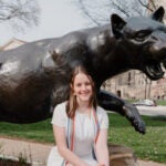 Woman with brown hair wearing a white dress in front of a panther statue.