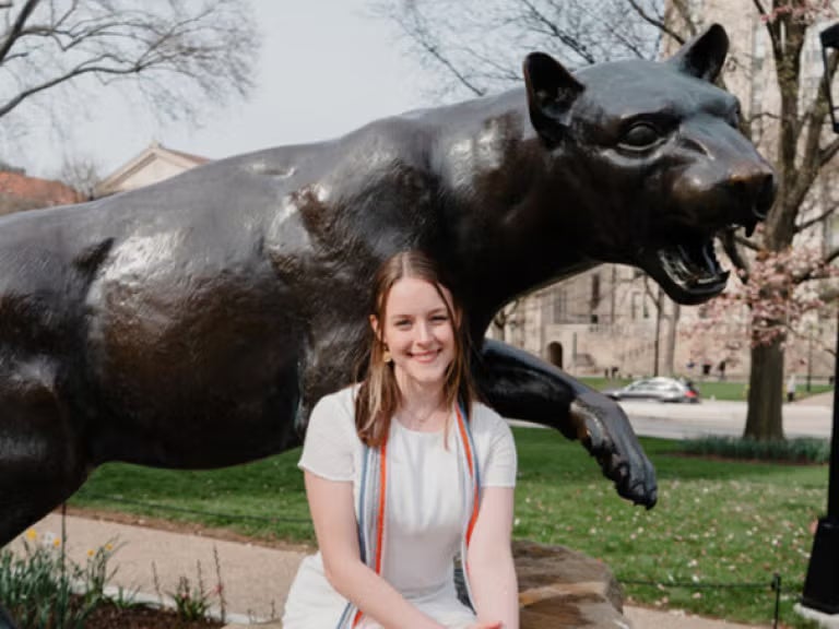 Woman with brown hair wearing a white dress in front of a panther statue.