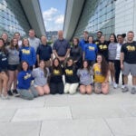 A group of men and women wearing Pitt shirts gathered together outside.