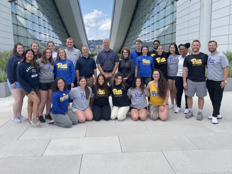 A group of men and women wearing Pitt shirts gathered together outside.