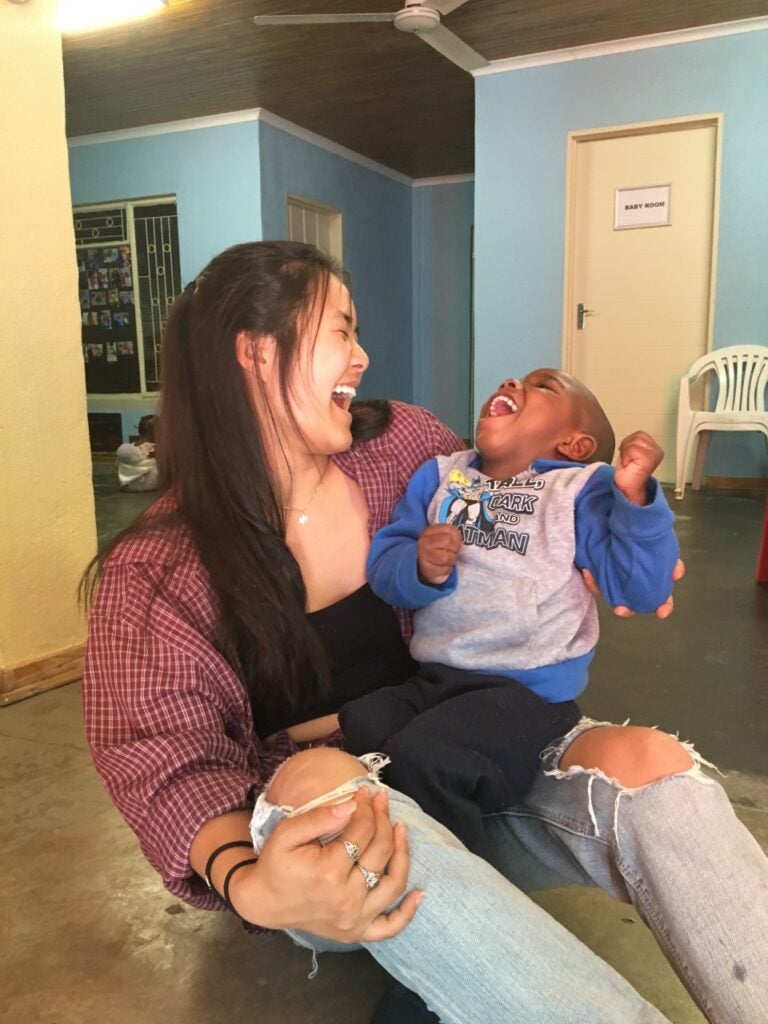 Woman with long brown hair wearing a red flannel shirt over a black top and jeans while holding a little boy who is wearing a blue and gray sweatshirt and black pants.