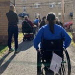 A group of people sitting in wheelchairs outside.