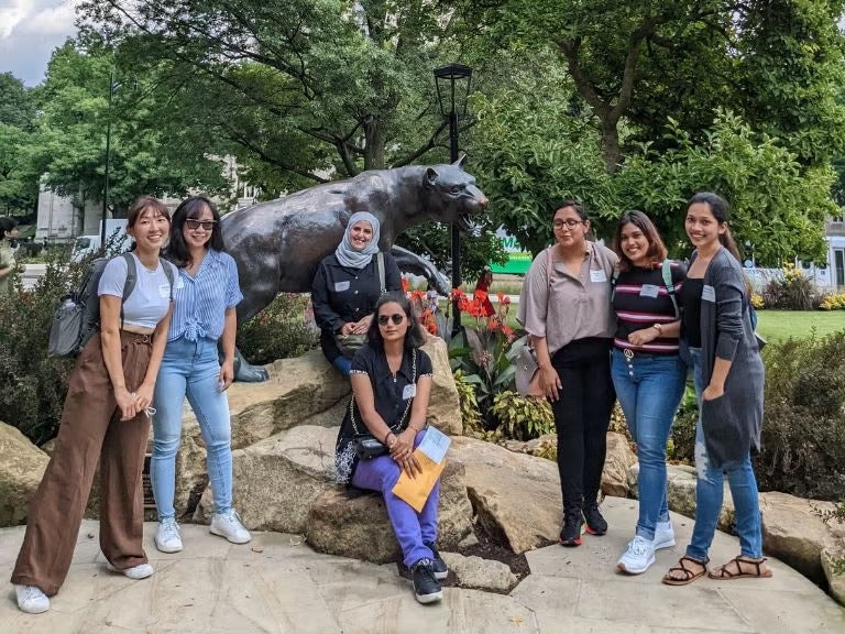 A group of women standing together outside near a panther statue.