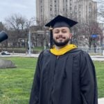 Man with a short beard wearing a black graduation cap and gown.