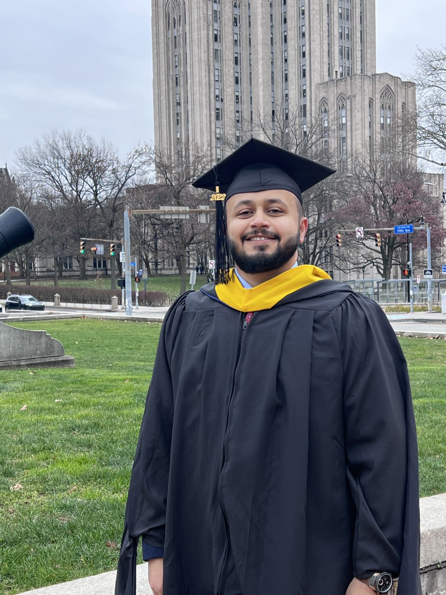 Man with a short beard wearing a black graduation cap and gown.