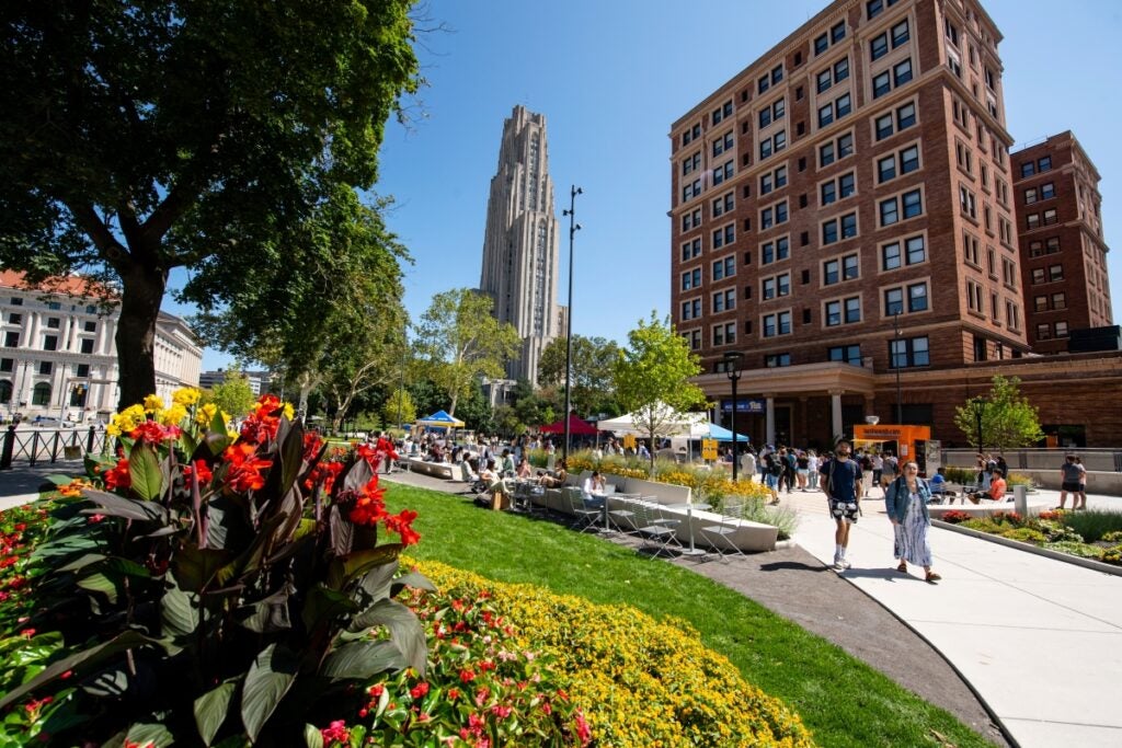 A view of campus with the Cathedral of Learning and William Pitt Union with students gathering and walking together.