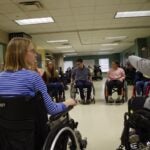 A group of men and women sitting in wheelchairs in a circle talking to one another.