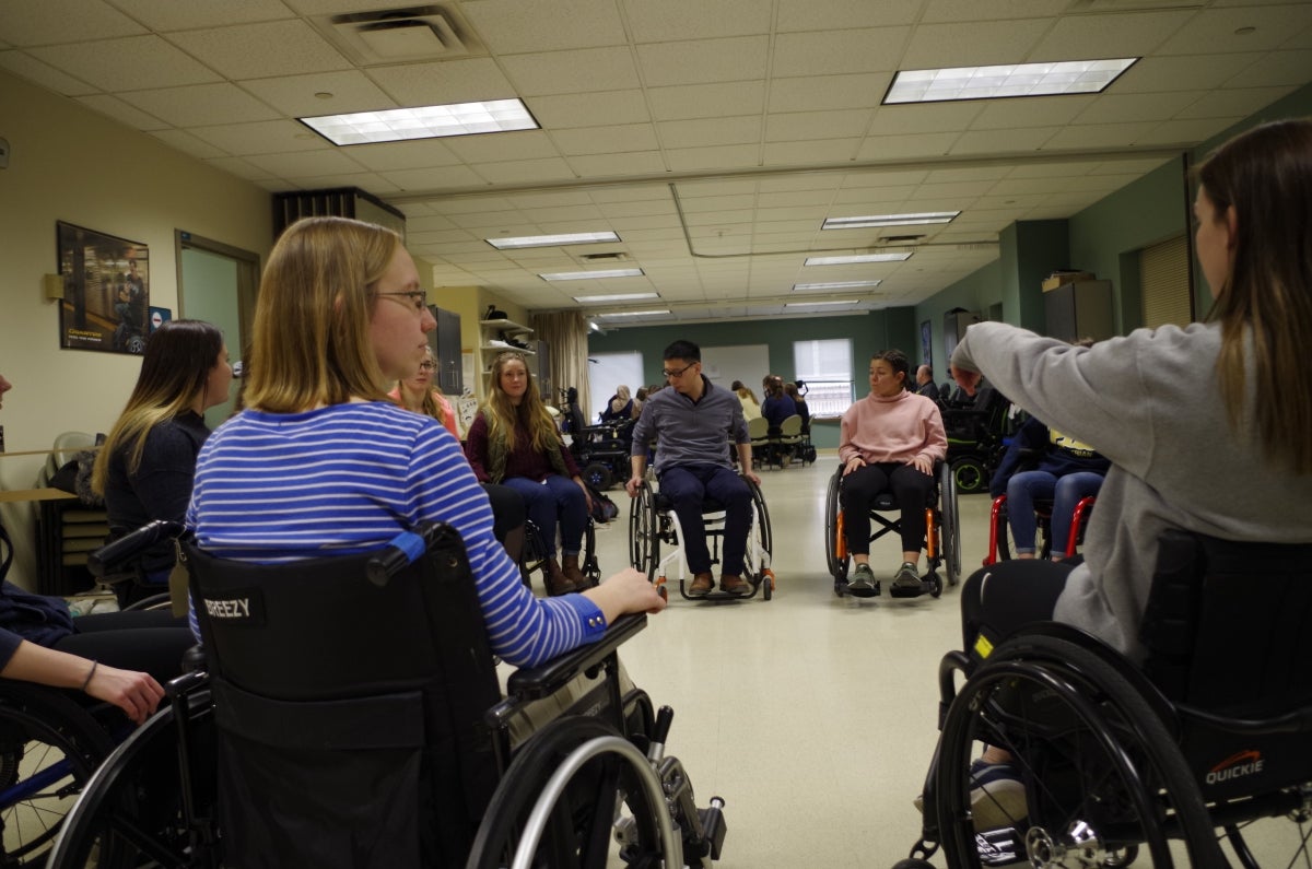 A group of men and women sitting in wheelchairs in a circle talking to one another.