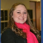 A woman with long brown hair wearing a hot pink scarf over a black sweater.