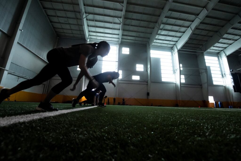 Two people wearing dark clothing running on turf.