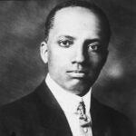 An aged black and white portrait of a man with dark skin and cropped black hair wearing a suit and tie