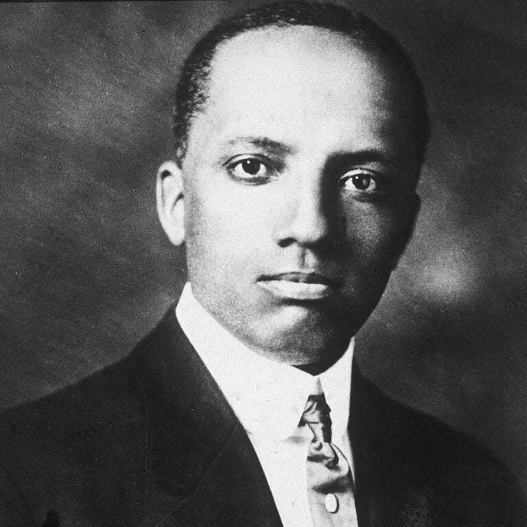 An aged black and white portrait of a man with dark skin and cropped black hair wearing a suit and tie